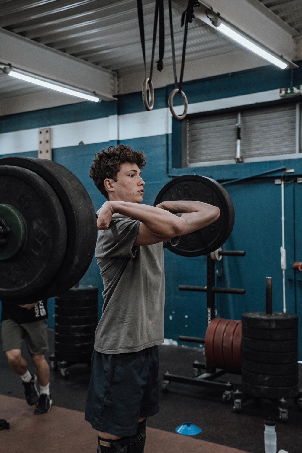 A teenage athlete training with a barbell in the weight room